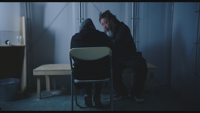 Ai Weiwei sits with a woman in a refugee camp.