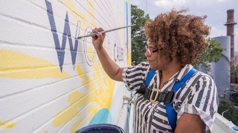 A few days ahead of the mural’s dedication, Dove joined Guinn on scaffolding high above the corner to fill in the last unpainted word, “world.”