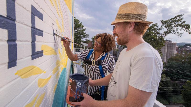 A few days ahead of the mural’s dedication, Dove joined Guinn on scaffolding high above the corner to fill in the last unpainted word, “world.”
