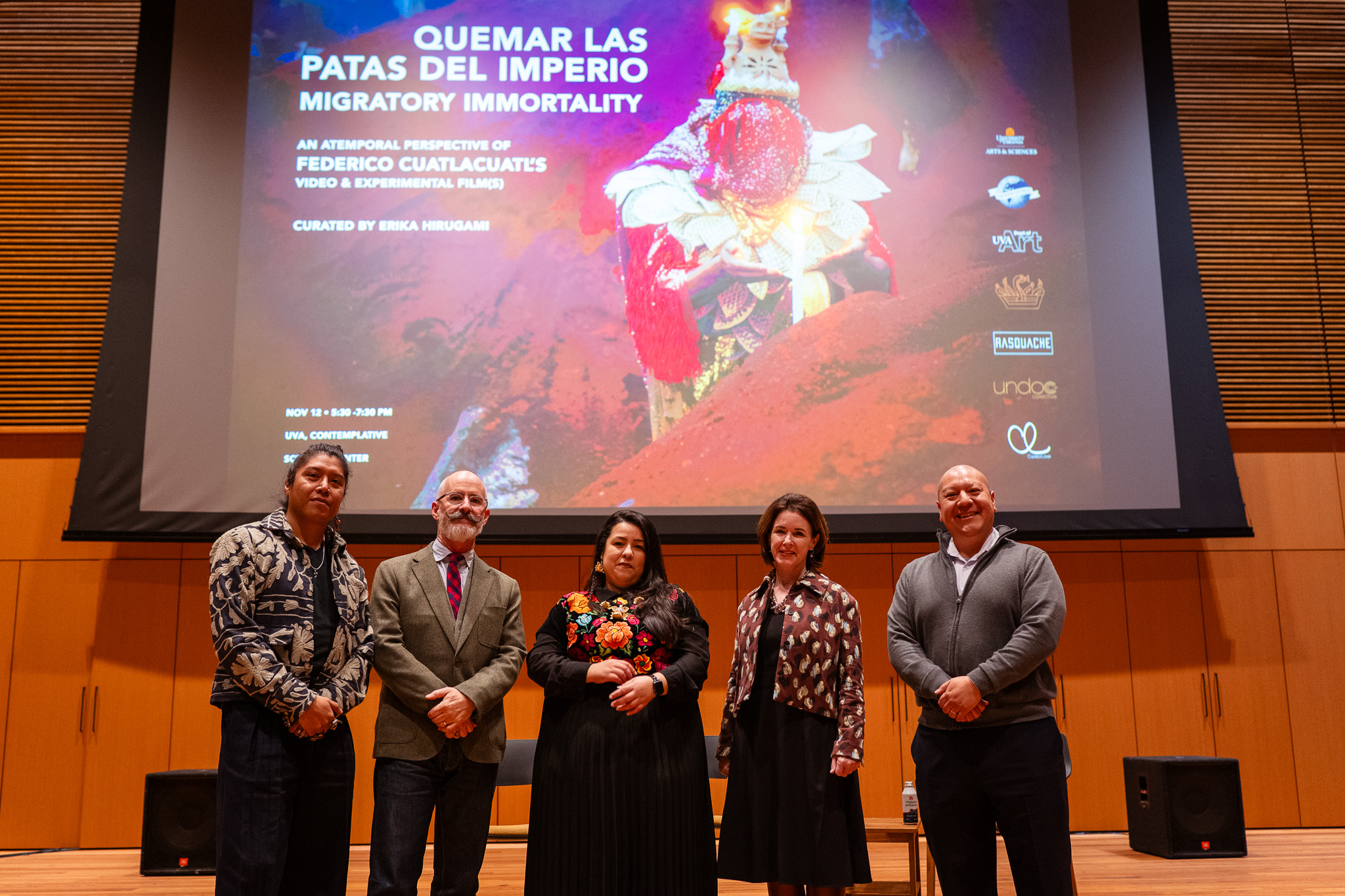 Five featured speakers at the Nov. 12 Enabling Difficult Conversations film screening stand on stage in front of a large screen featuring an image from one of Federico Cuatlacuatl's experimental films.