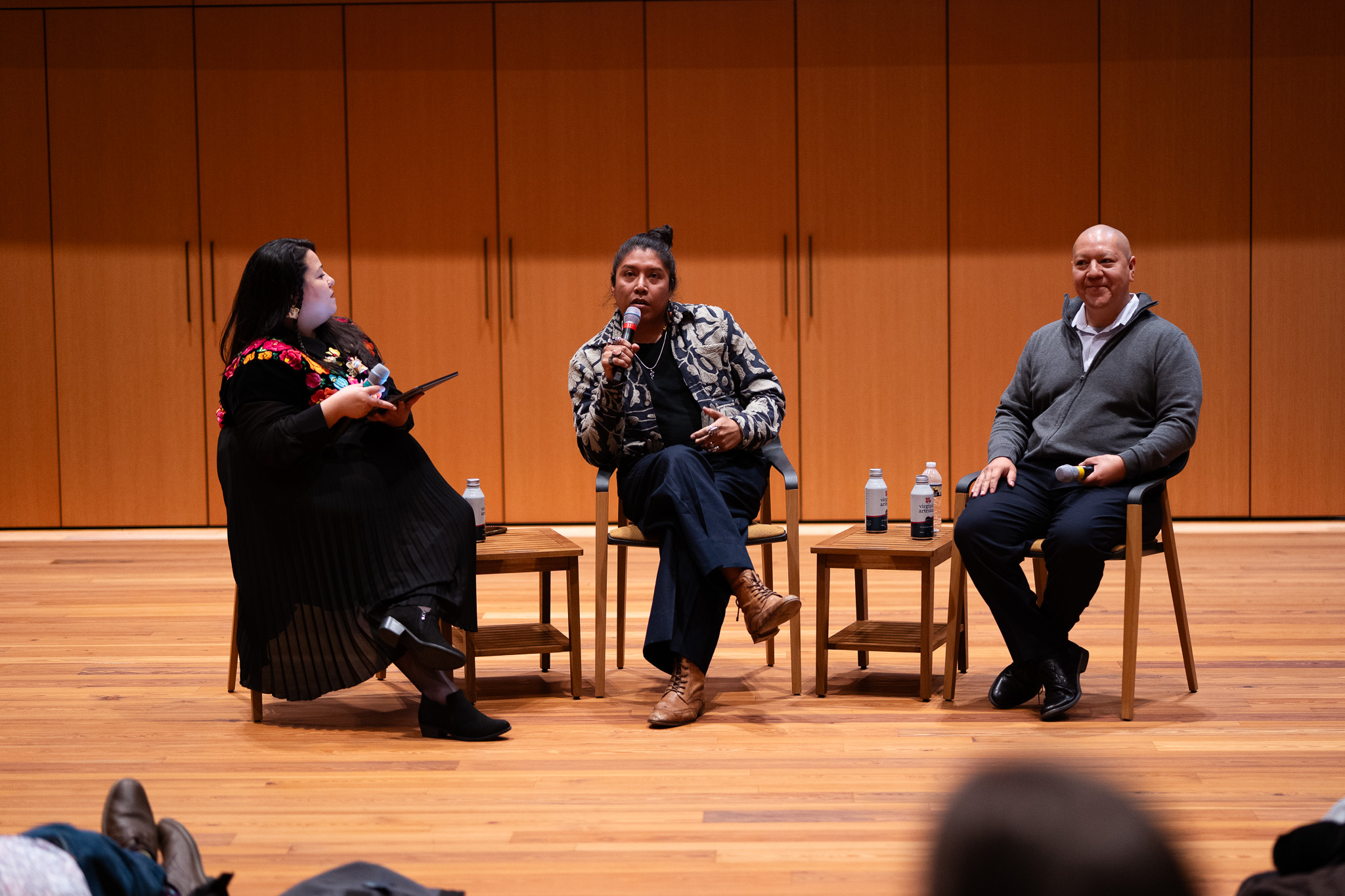 Federico Cuatlacuatl speaks into microphone during panel discussion as two other panelists listen.