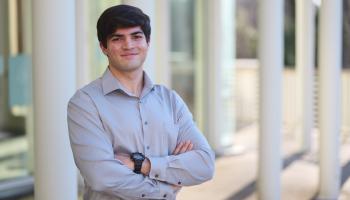 Smiling college student stands with arms crossed across his chest.