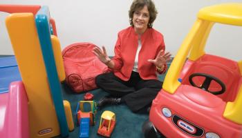 Psychology professor Judy Deloache sitting cross-legged on the floor surrounded by children's toys.